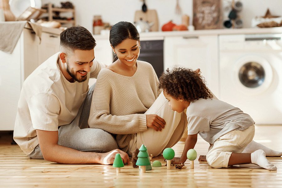 Personal Insurance - A Happy Father and Mother are Sitting on the Floor With Their Son Playing With Toys at Home