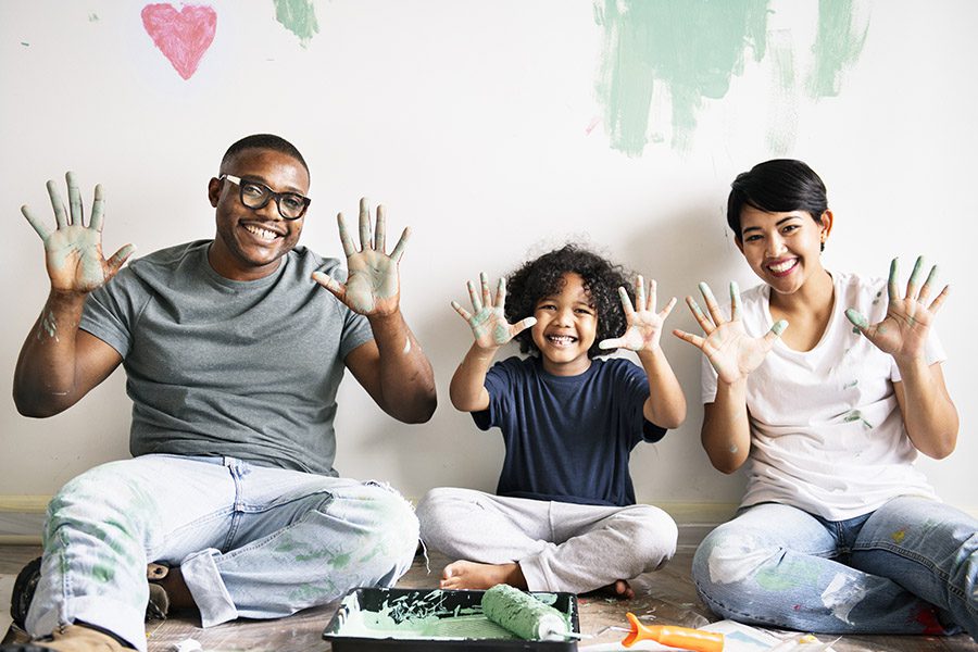 Blog - Happy Father, Mother and Child Have Their Painted Hands Out as They Playfully Paint a Wall