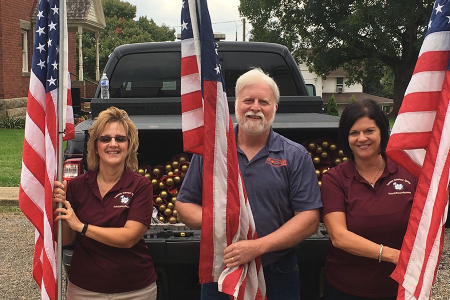 About Our Agency - Denise, Trisha, and a Colleague Standing Together in Front of a Pick-up Truck Holding American Flags